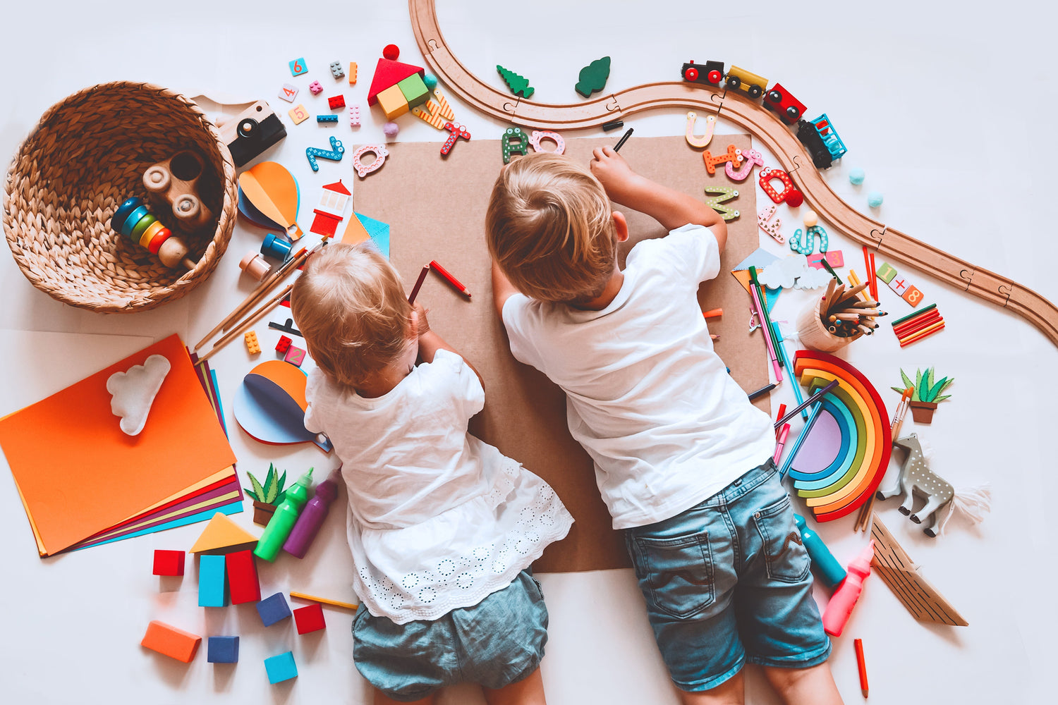 Two children engaging in creative play with Montessori-inspired toys, art supplies, and a wooden train set. A hands-on learning environment promoting creativity, fine motor skills, and open-ended play. Ideal for Montessori and Waldorf-style education
