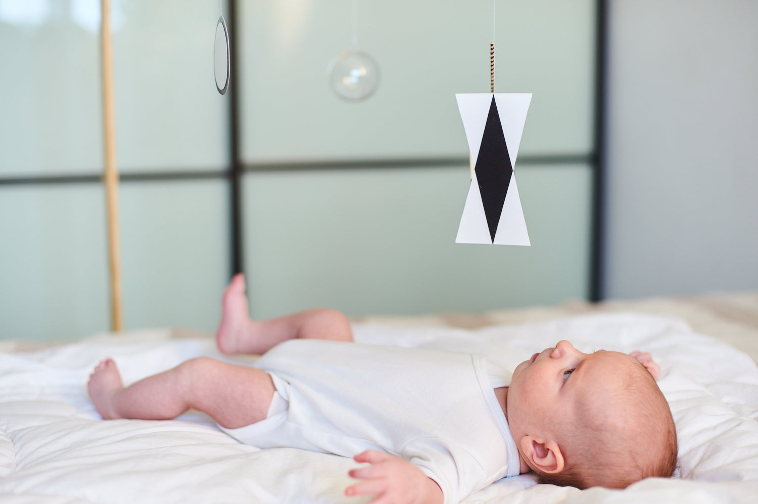 Montessori black and white baby mobile with high-contrast geometric shapes, designed to support newborn visual development. A baby lies on a soft bed, gazing at the sensory mobile. Ideal for Montessori-inspired nurseries and early infant stimulation.