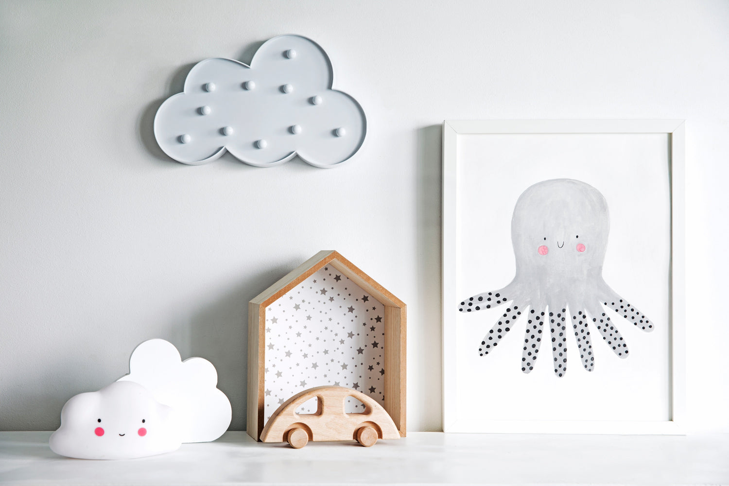 Minimalist nursery decor with wooden toys, cloud-themed accents, and a framed octopus illustration. Neutral Montessori-inspired baby room design promoting a calming and playful environment